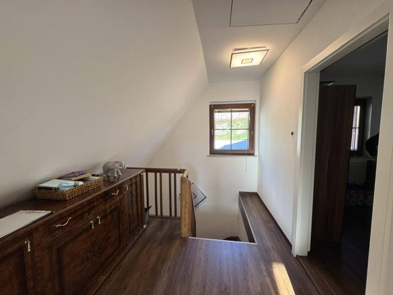 Heller Flur im Obergeschoss mit Holzboden, Fenster und Zugang zu weiteren Räumen.