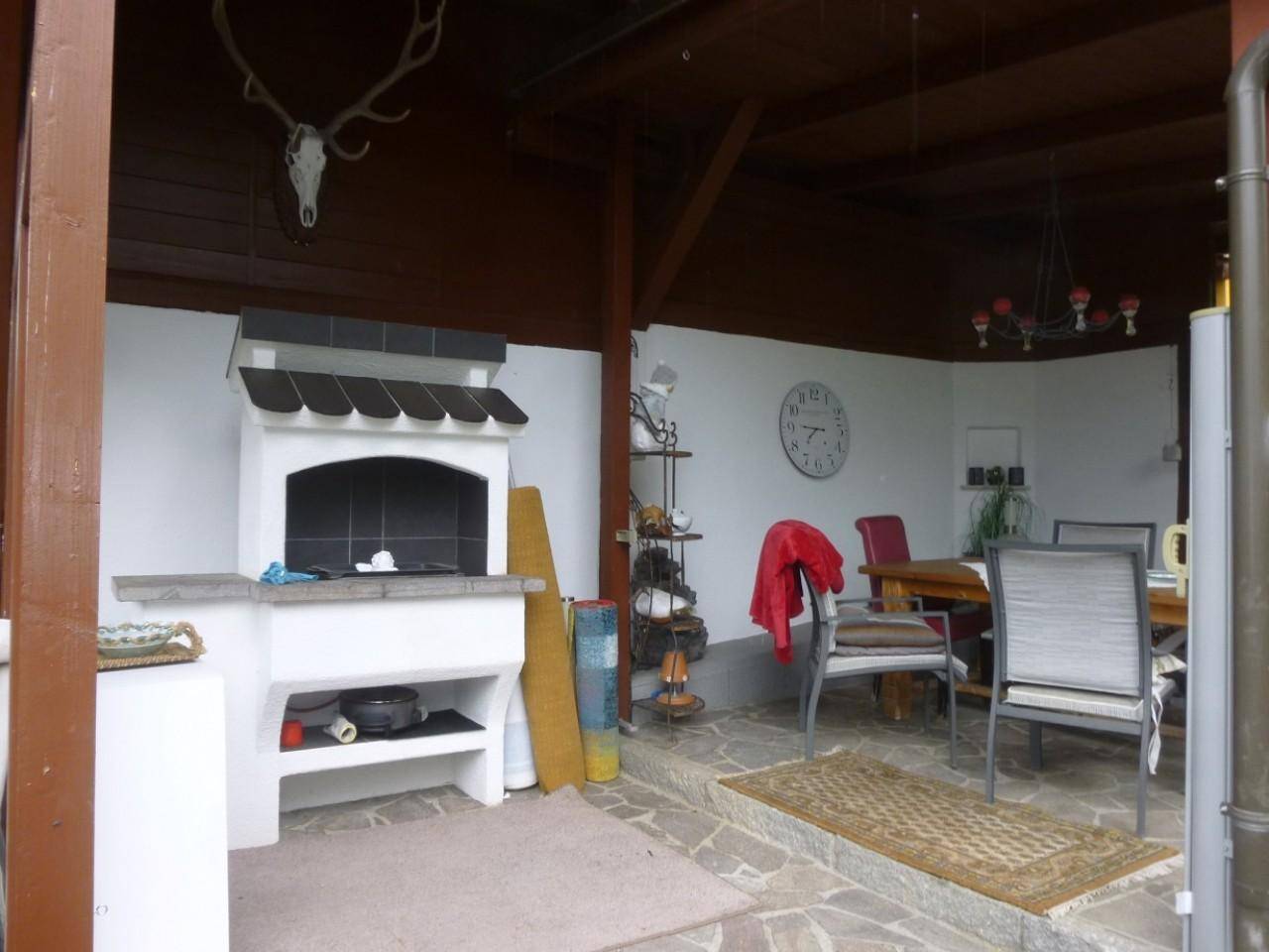 Überdachte Terrasse mit Grillplatz, Esstisch und rustikalem Ambiente.