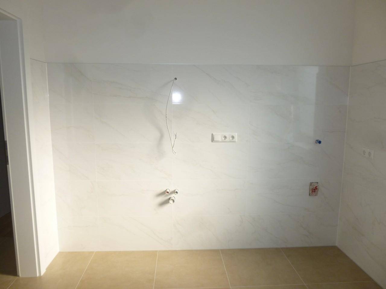Badezimmer im Bau mit hellen Fliesen und Anschlüssen für Waschtisch und Dusche.