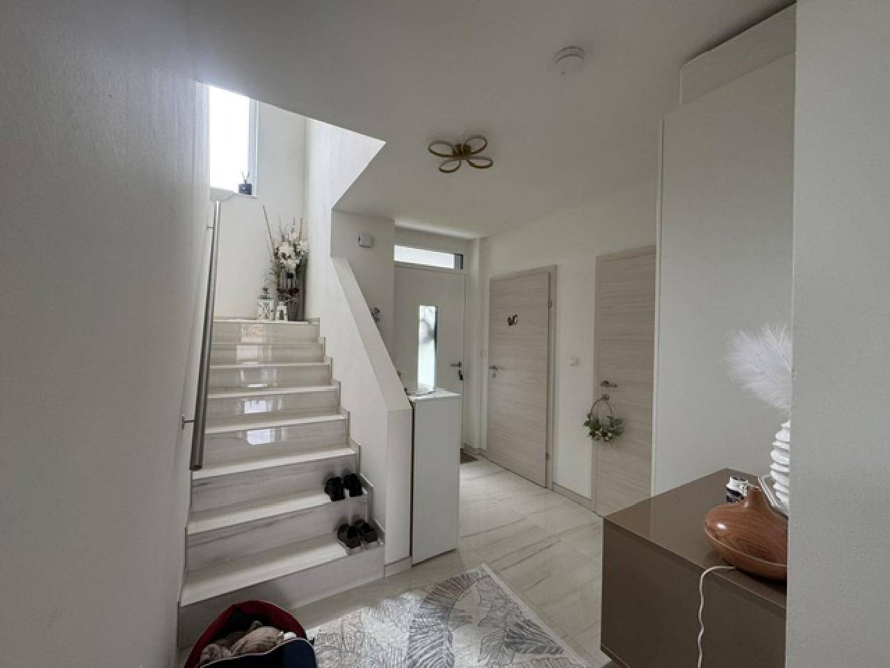 Heller Eingangsbereich mit moderner Treppe und Zugang zu weiteren Räumen.