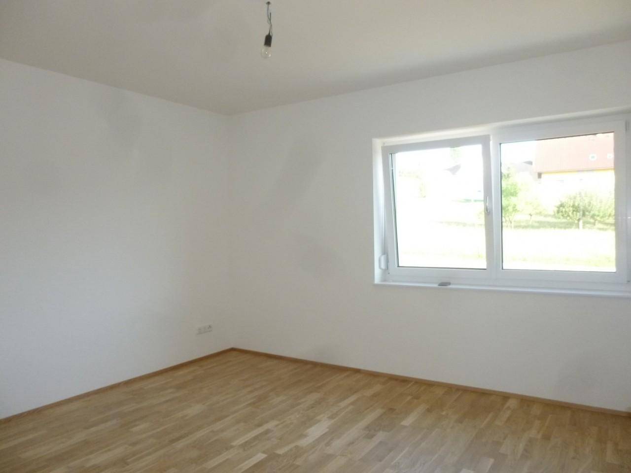 Geräumiges leeres Zimmer mit Holzparkett und großem Fenster für viel Tageslicht.