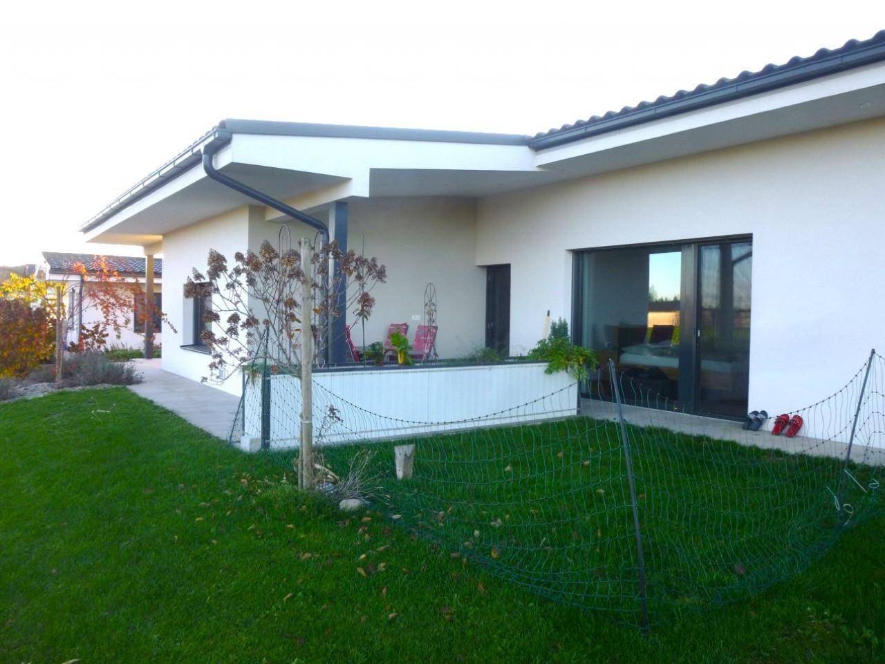 Überdachte Terrasse mit Zugang zum Garten und großen Glasfronten, umgeben von Grünflächen.