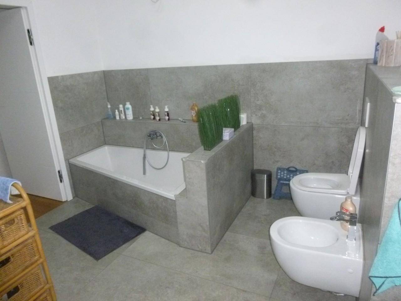 Modernes Badezimmer mit Badewanne, WC und Bidet, ausgestattet mit grauen Fliesen.