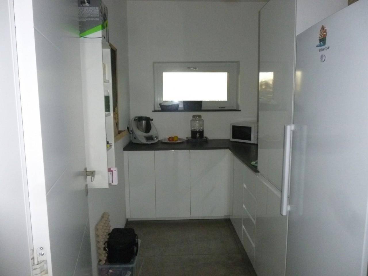 Funktionale Küche mit weißen Schränken, Arbeitsplatte und Fenster, ideal als Speisekammer.