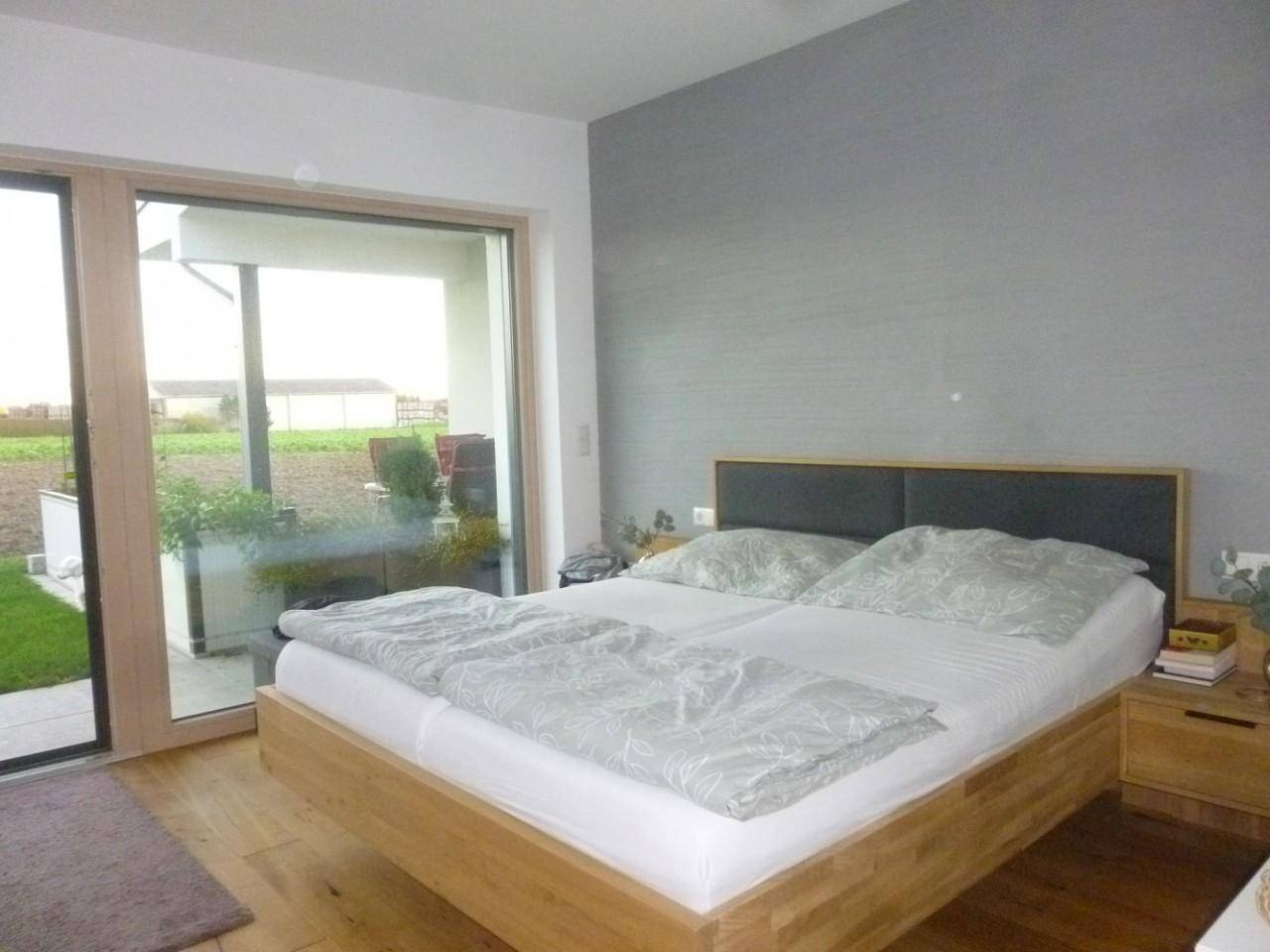 Schlafzimmer mit Holzbett, Parkettboden und Zugang zu einer Terrasse mit Blick ins Grüne.