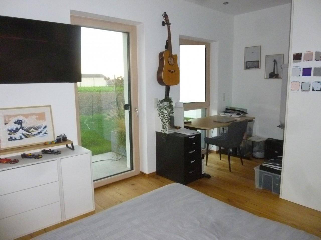 Geräumiges Zimmer mit Holzboden, Schreibtisch und Zugang zum Garten durch eine Terrassentür.