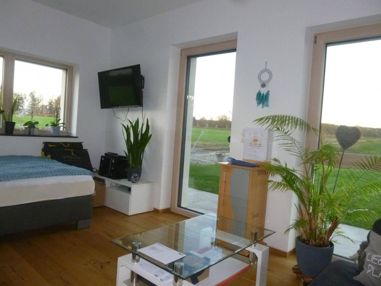 Helles Zimmer mit Holzboden, großen Fenstern und Blick auf die umliegende Landschaft.