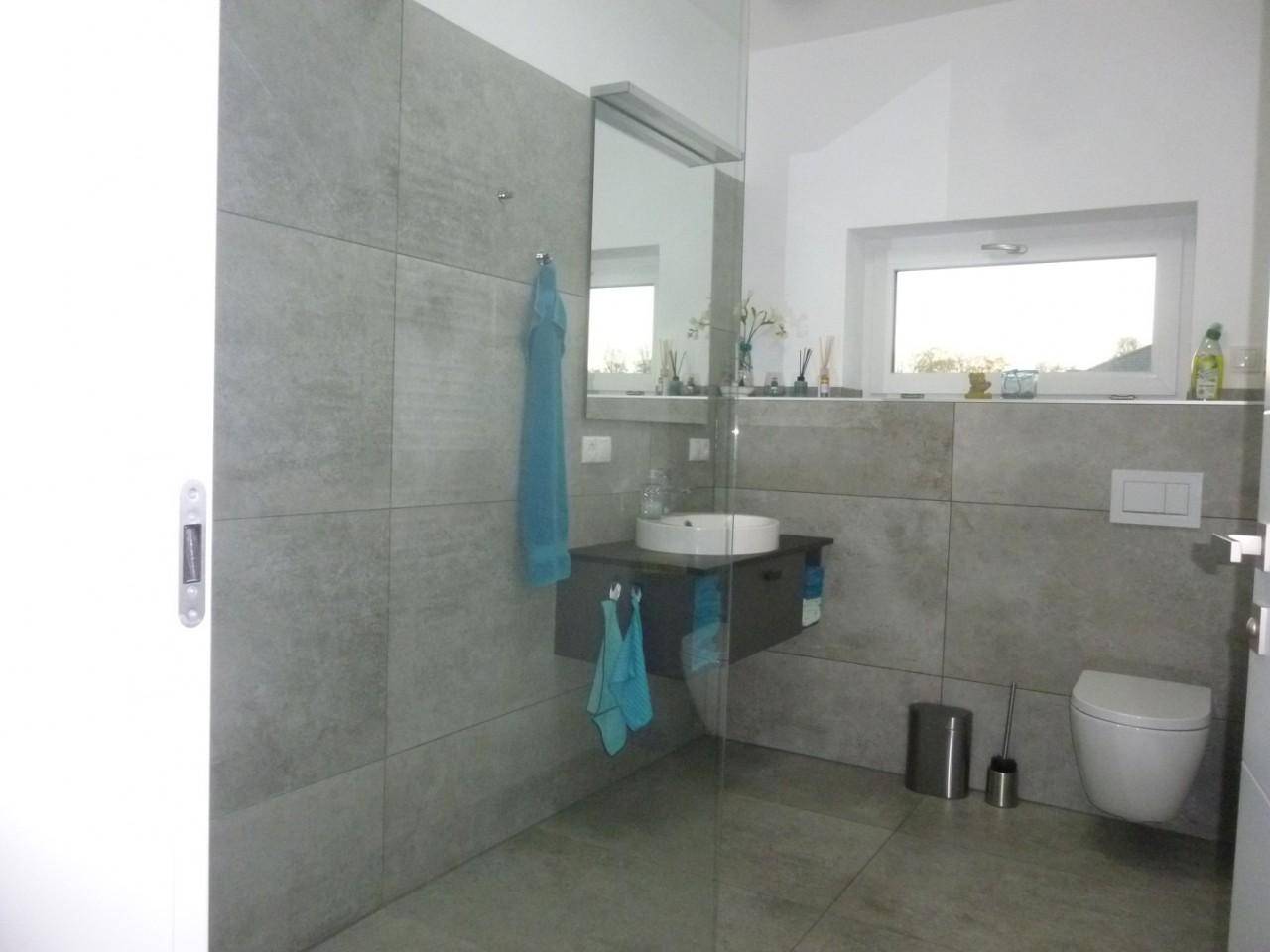 Modernes Badezimmer mit Dusche, Waschtisch und WC, hell gefliest und mit Fenster.