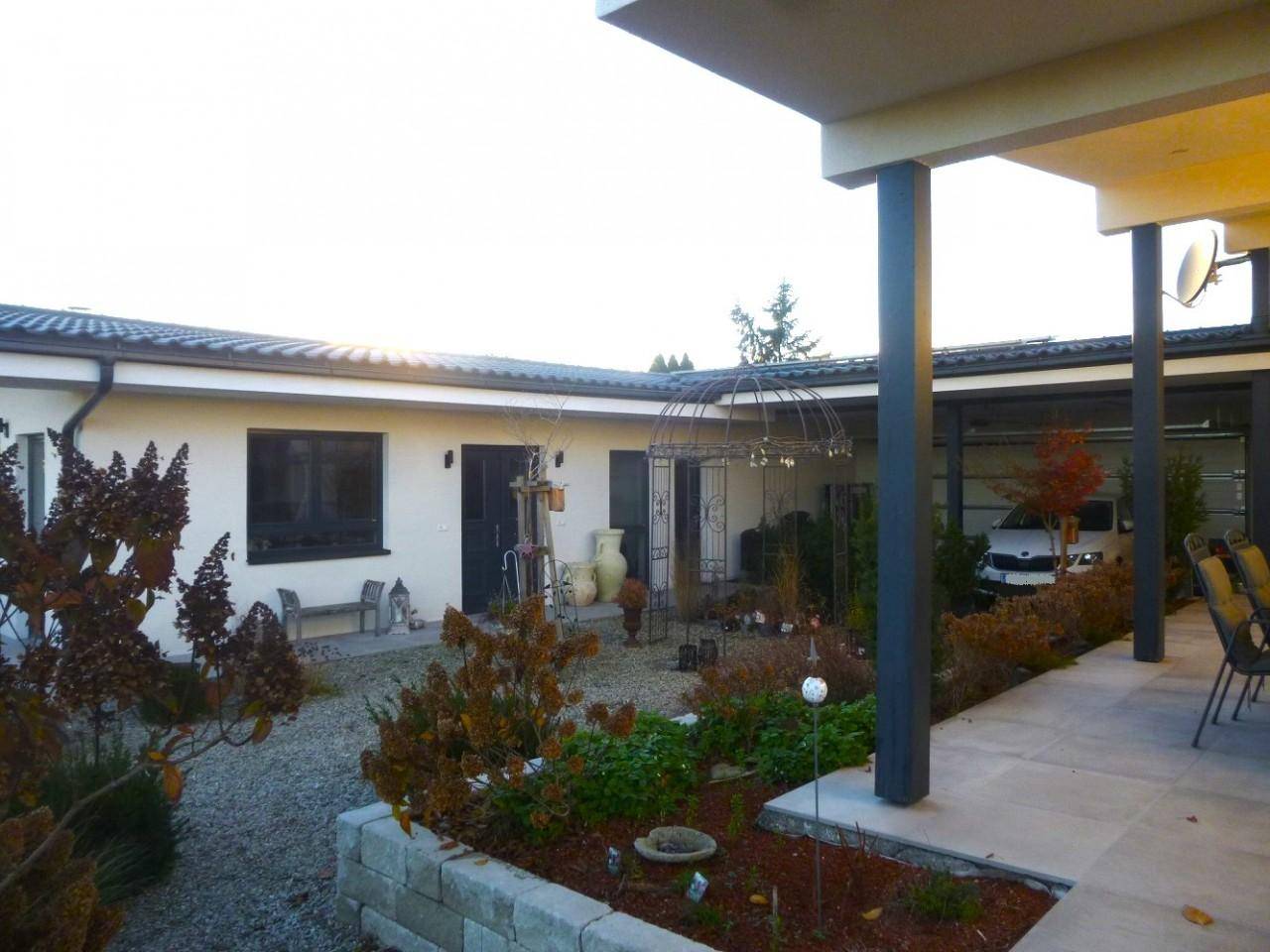 Innenhof mit gepflegtem Gartenbereich, überdachtem Carport und Sitzgelegenheiten im Freien.