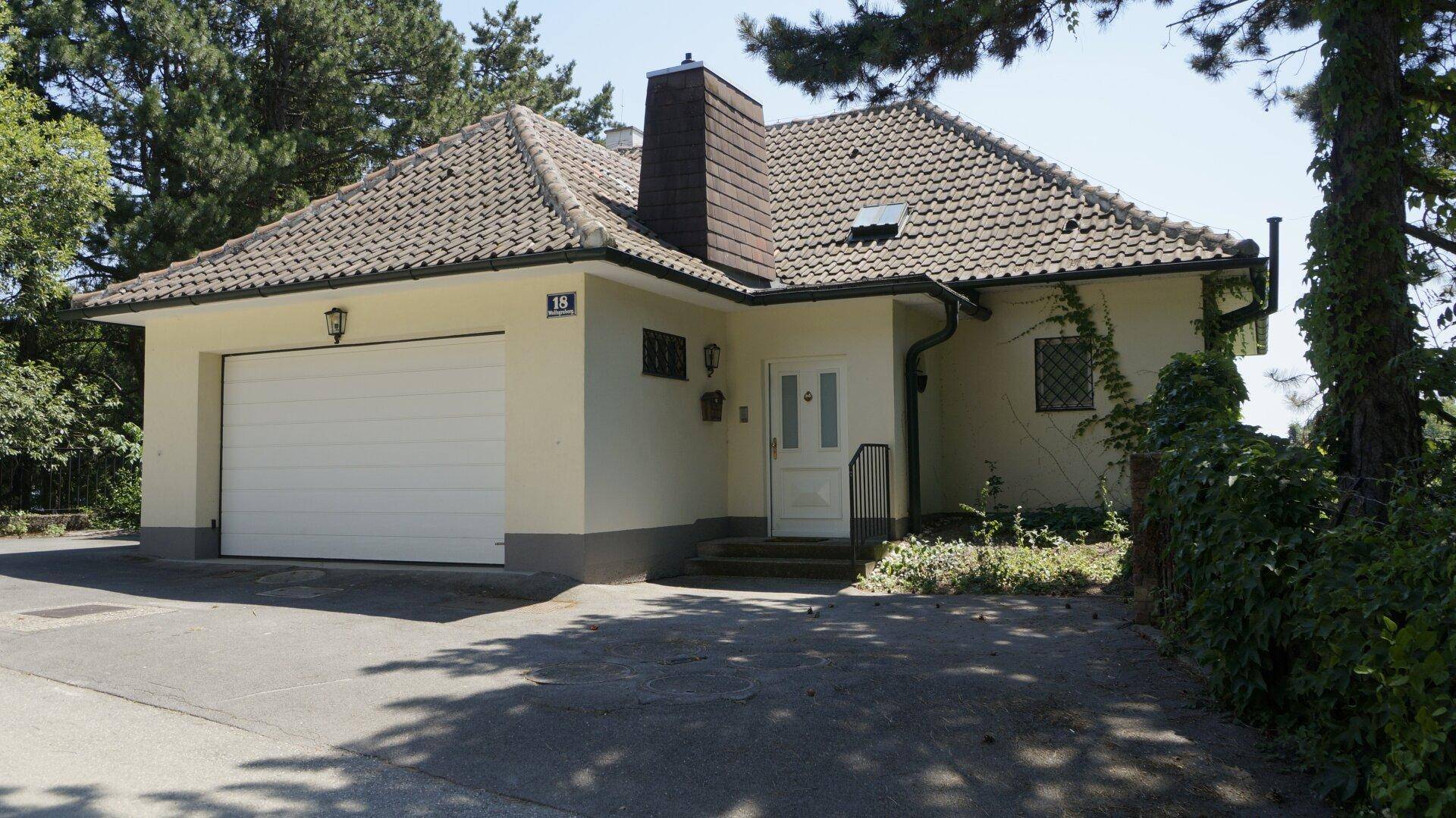 Hauseingang mit großer Garage und gepflasterter Auffahrt umgeben von Grün.