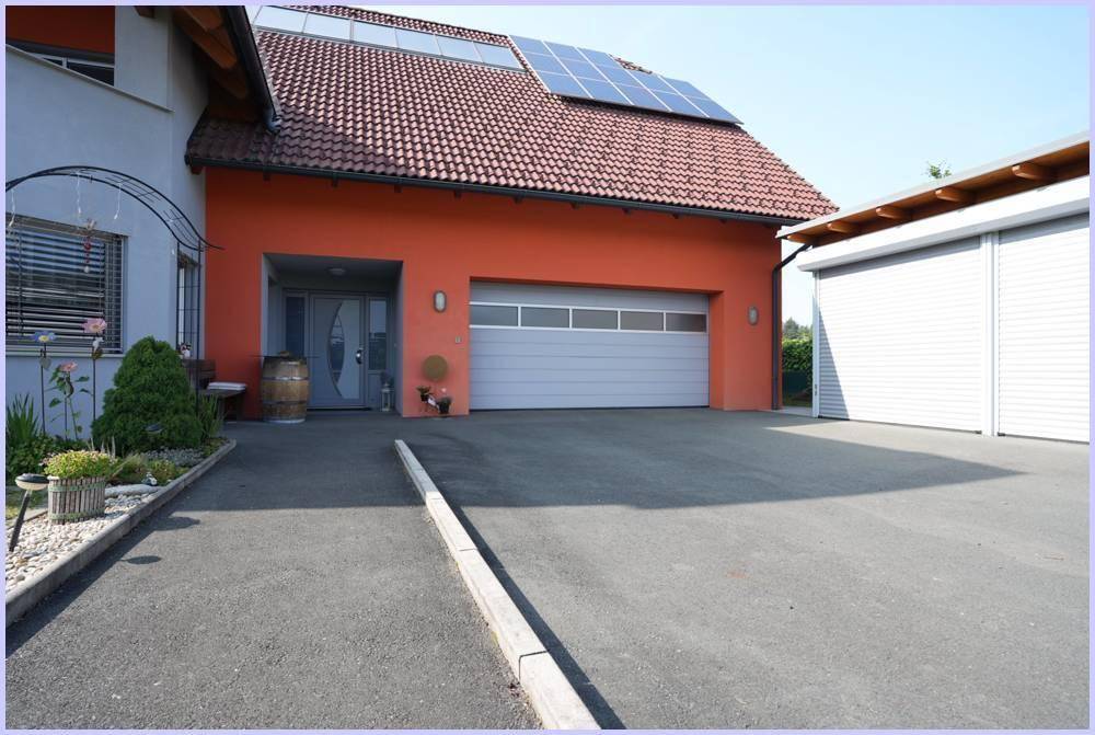 Haus mit oranger Fassade, Garage, Auffahrt und Solaranlage auf dem Dach.