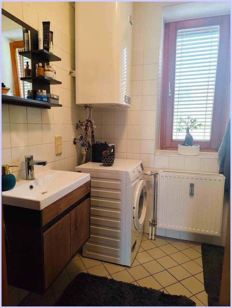 Badezimmer mit Waschbecken, Waschmaschine, Boiler und Fenster.