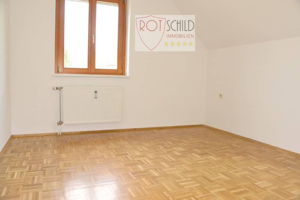 Helles Schlafzimmer mit Parkettboden, Dachschräge und Fenster.