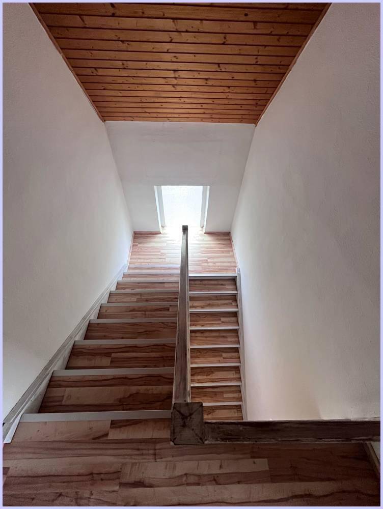 Holztreppe mit Holzdecke und einem Dachfenster, das natürliches Licht spendet.