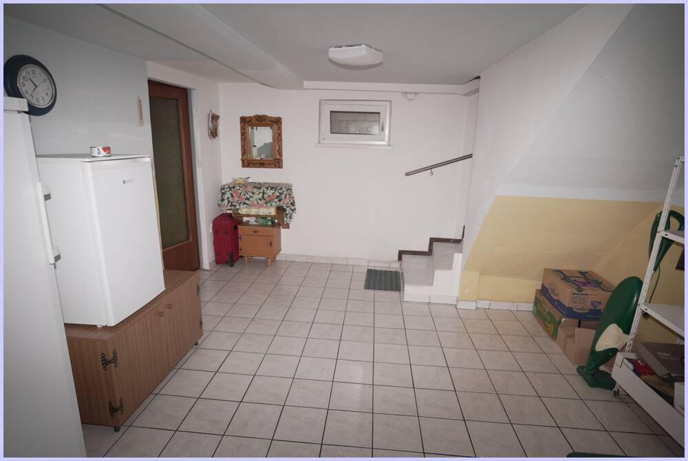 Kellerraum mit Fliesenboden, Kühlschrank und Treppenaufgang.