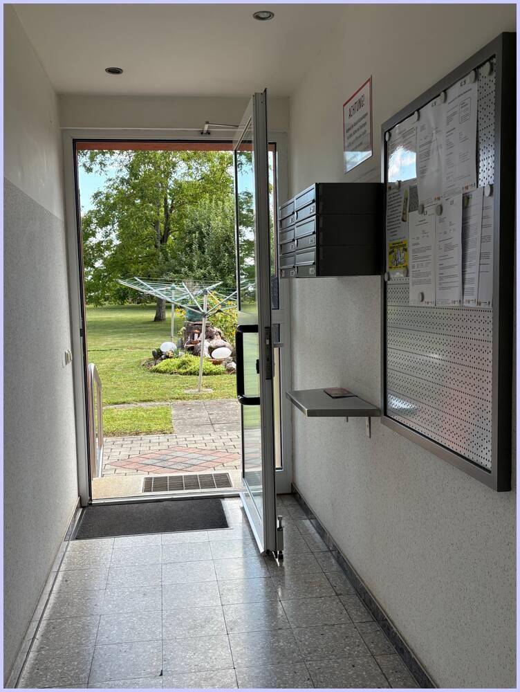 Eingangsbereich mit Blick ins Grüne, schwarzem Briefkasten und Informationswand.