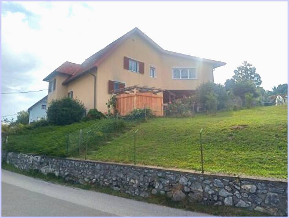 Einfamilienhaus mit gelber Fassade und Satteldach auf einem Hanggrundstück.