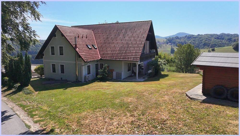 Seitenansicht des Hauses mit hellgrüner Fassade, rotem Dach und einem kleinen Holzschuppen im Vordergrund.