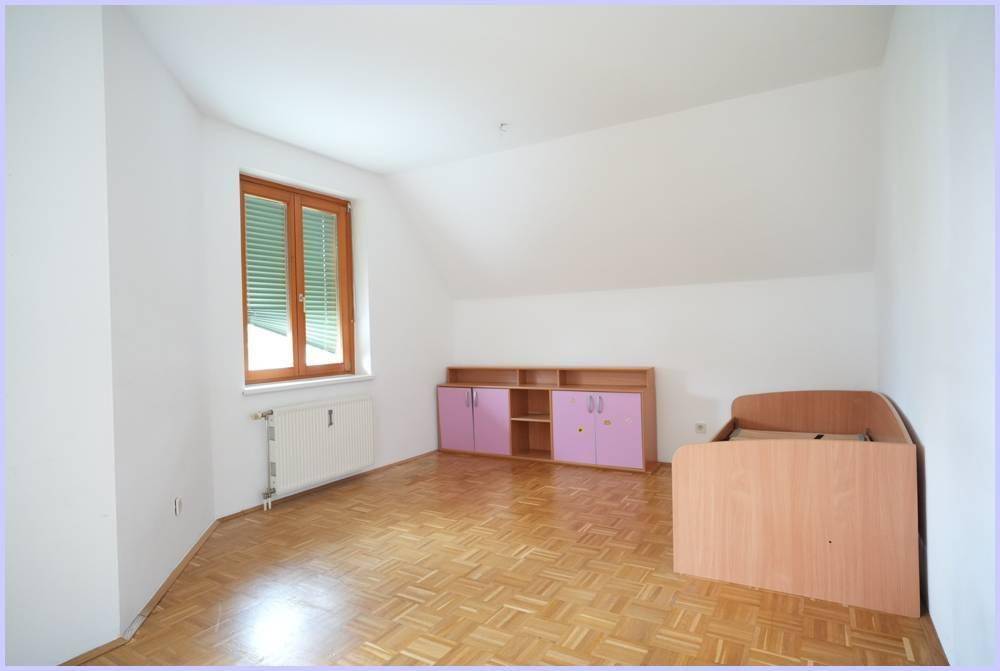 Schlafzimmer mit Parkettboden, Fenster und Möbeln in hellem Holz und Lila.