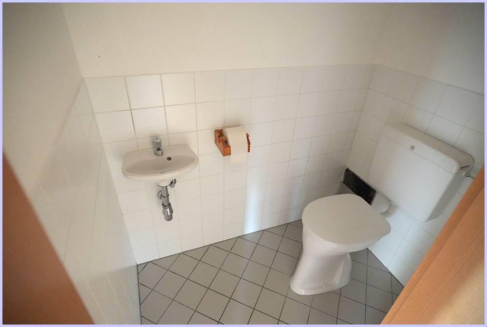 Kleines Gäste-WC mit Toilette, Waschbecken und Fliesenboden.