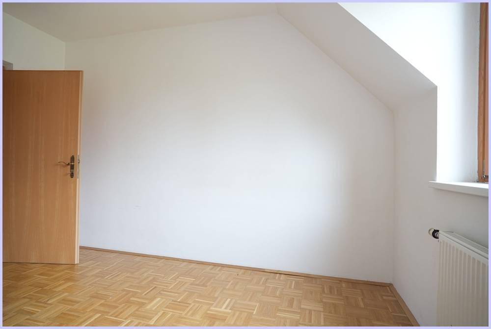 Leerer Raum mit Parkettboden, Holztür und schräger Wand, ideal für ein Schlafzimmer.