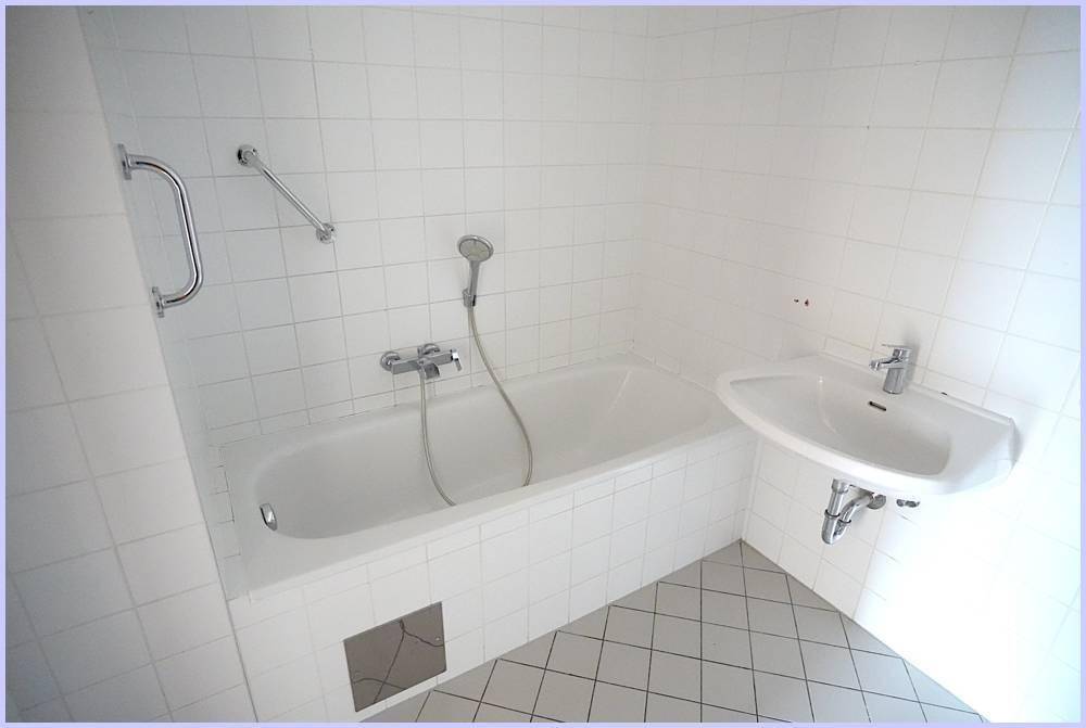 Gefliestes Badezimmer mit Badewanne, Waschbecken und Haltegriffen für mehr Sicherheit.