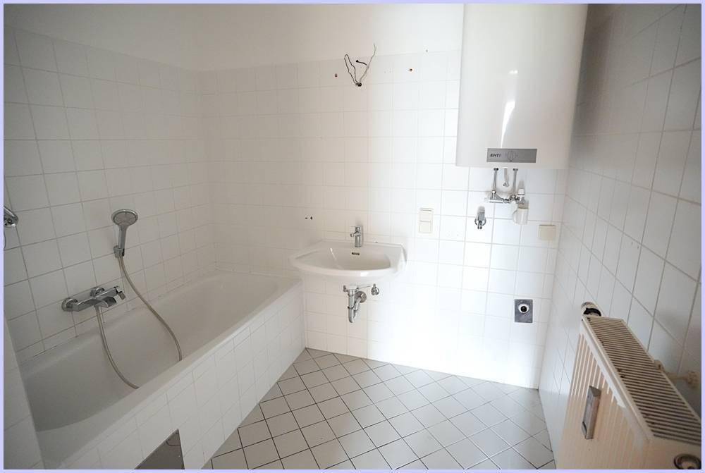 Helles Badezimmer mit Badewanne, Waschbecken und Boiler an der Wand.
