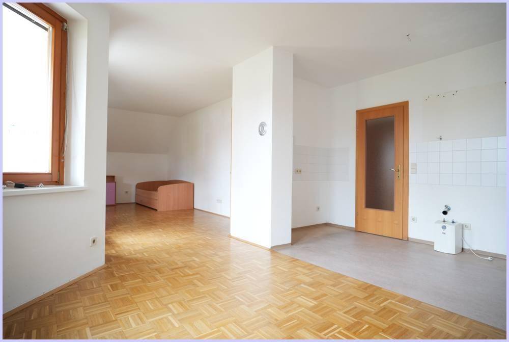 Heller offener Wohnbereich mit Parkettboden und vorbereiteter Küchenzeile an der Wand.