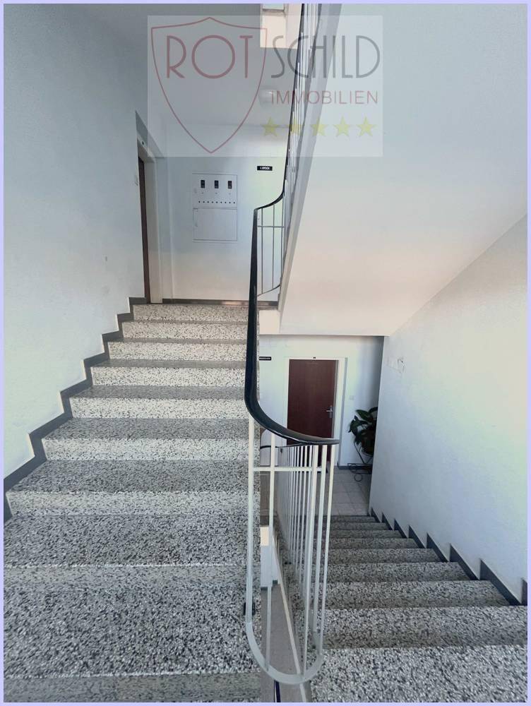 Geräumiges Treppenhaus mit hellen Wänden und einem eleganten Metallgeländer, das nach oben führt.
