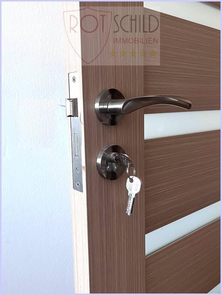 Moderne Holztür mit Metallgriff und Schlüssel im Schloss, die den Zugang zum Raum ermöglicht.