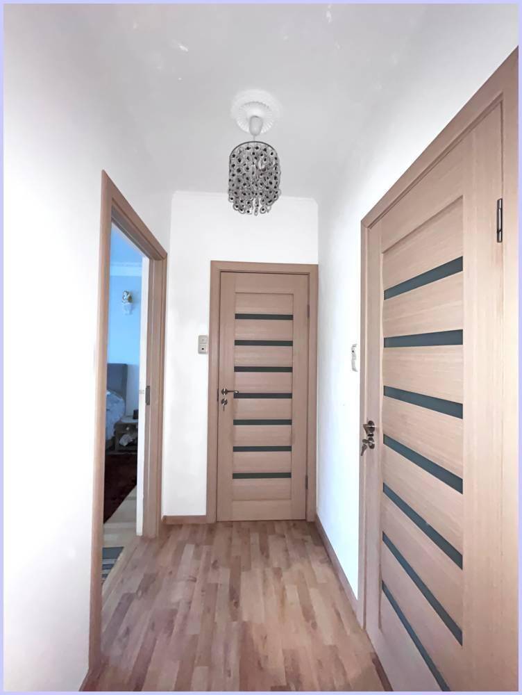 Schmaler Flur mit Laminatboden, hellen Holztüren und einer modernen Deckenleuchte.