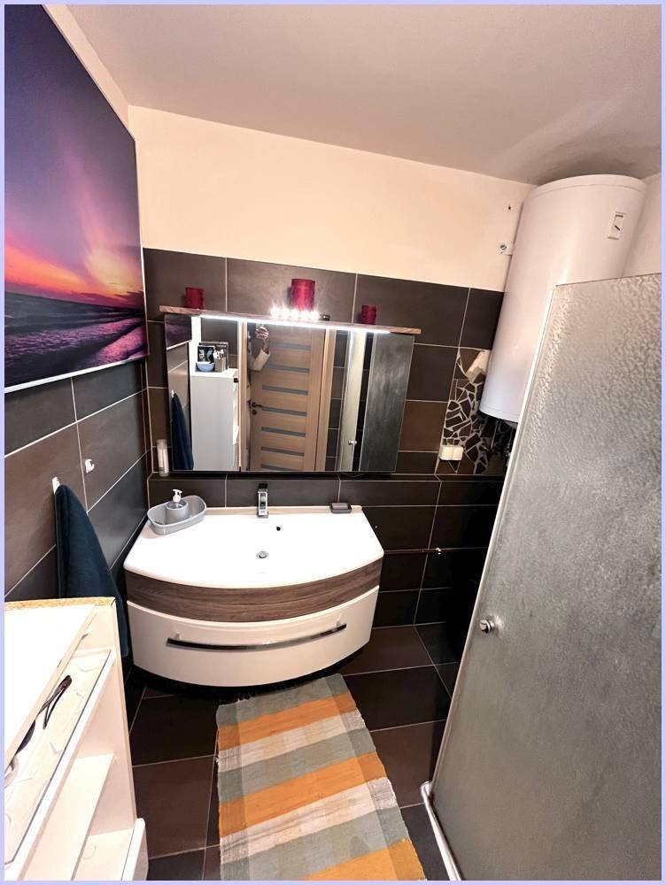 Modernes Badezimmer mit Waschtisch, Spiegelschrank und Duschkabine, dunkel gefliest.