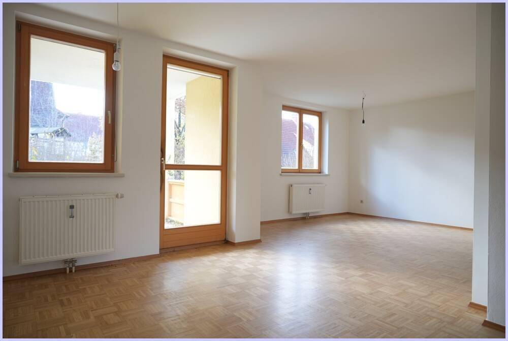 Geräumiges Wohnzimmer mit Parkettboden, großen Fenstern und Zugang zum Balkon.