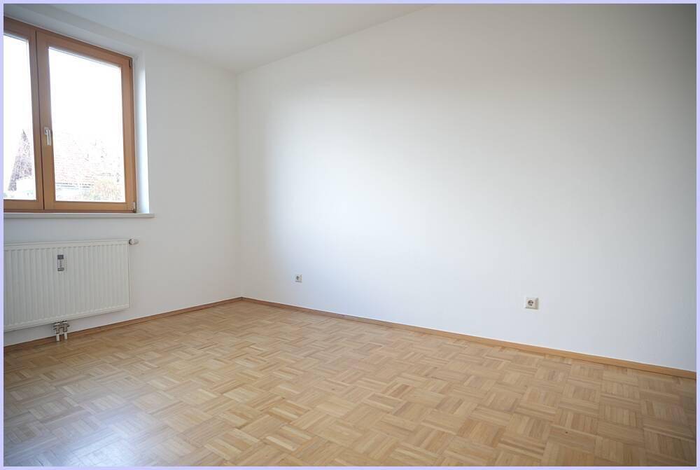 Helles Schlafzimmer mit Parkettboden und einem großen Fenster.