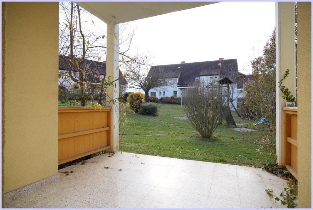 Überdachte Terrasse mit Fliesenboden und Blick auf den grünen Garten.
