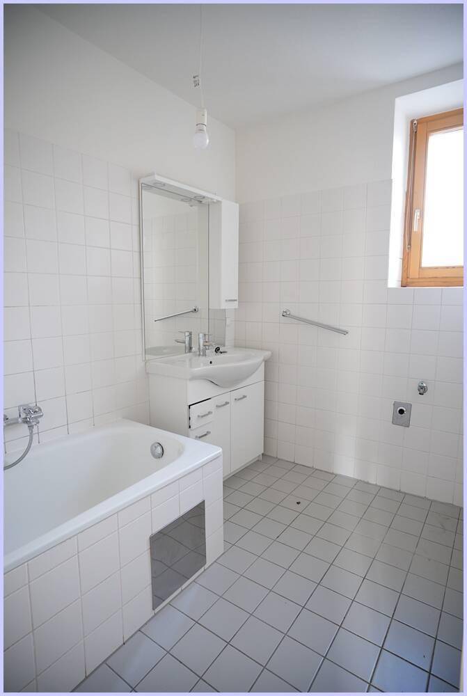 Helles Badezimmer mit Badewanne, Waschbecken, Spiegel und Fenster.