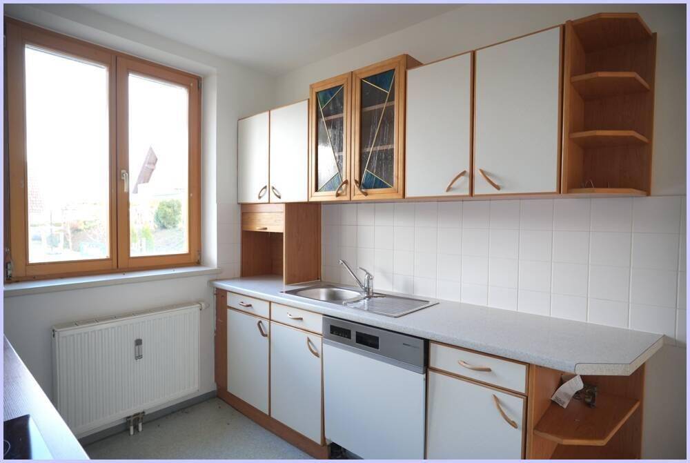 Helle Küche mit weißen Schränken, Spüle und Fensterblick ins Grüne.