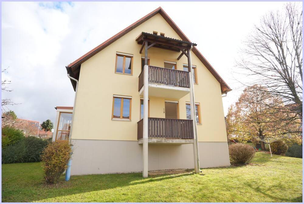 Rückansicht eines Mehrfamilienhauses mit zwei Balkonen und gepflegtem Rasen.