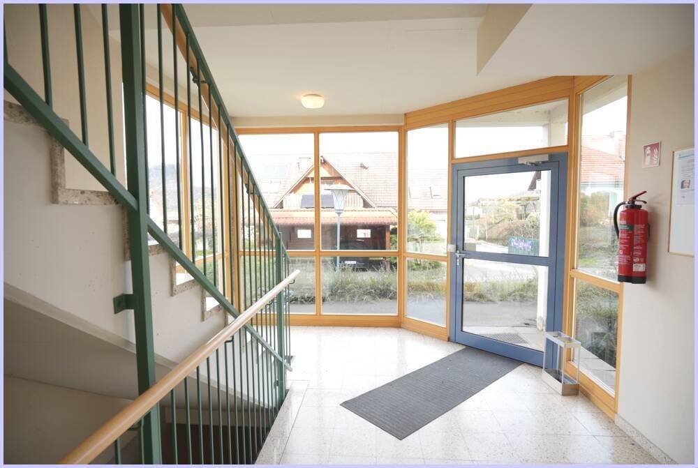Heller Eingangsbereich mit Treppenhaus, großen Fenstern und Zugang zum Außenbereich.