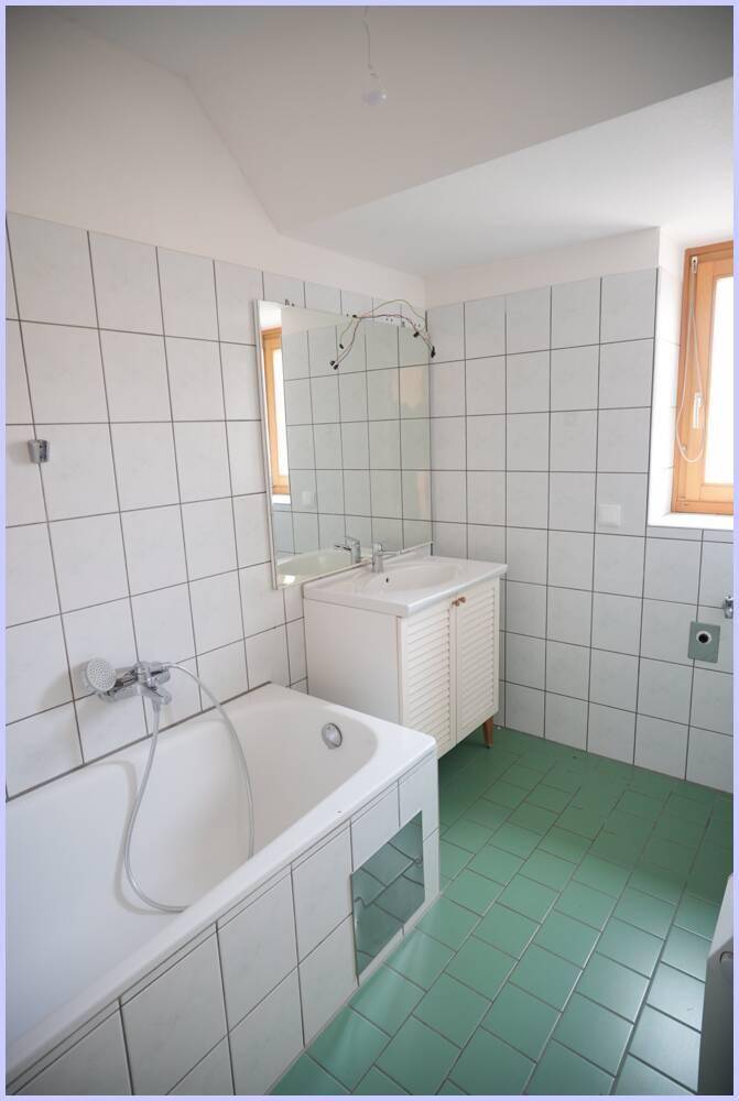 Badezimmer mit Badewanne, Waschbecken und weißen Wandfliesen, gut erhalten.