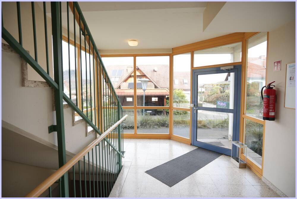 Heller Eingangsbereich mit Treppenhaus, großen Fenstern und Zugang zum Außenbereich.