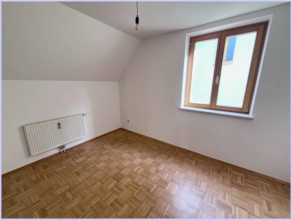 Leeres Zimmer mit Parkettboden, Dachschräge und Fenster, gut belichtet.