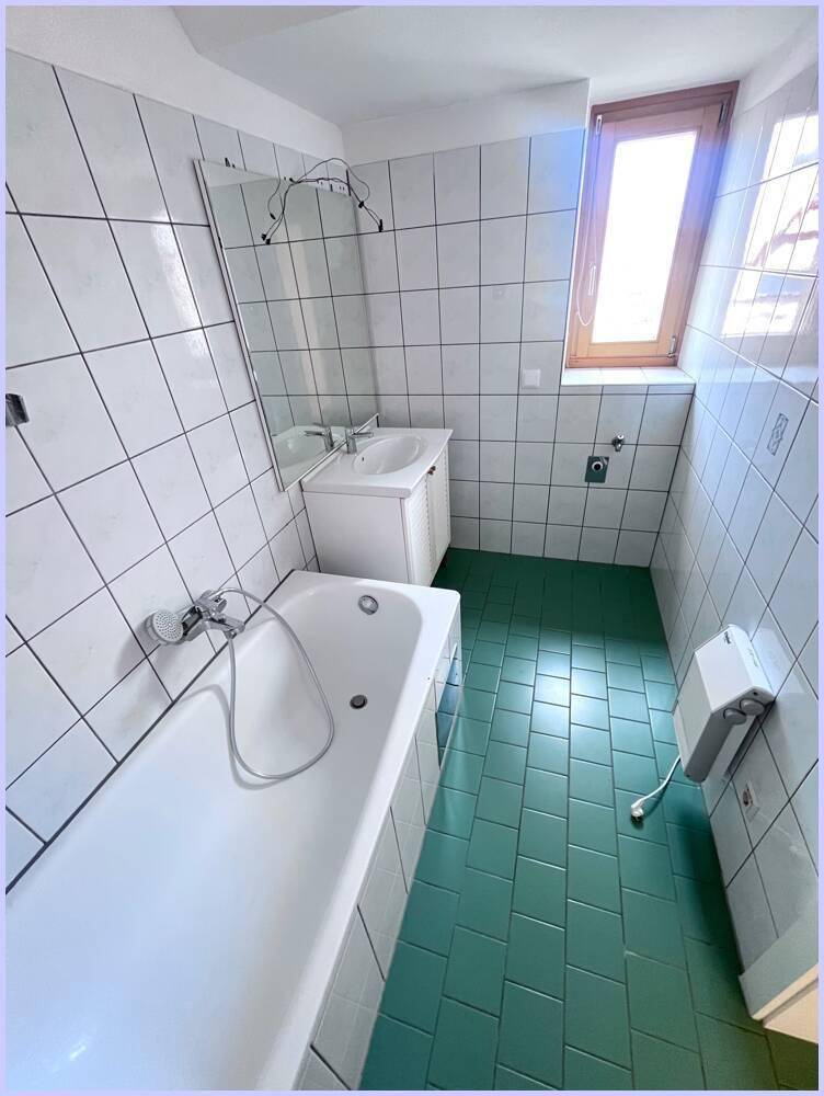Badezimmer mit Badewanne, Waschbecken, weißen Fliesen und grünem Boden.