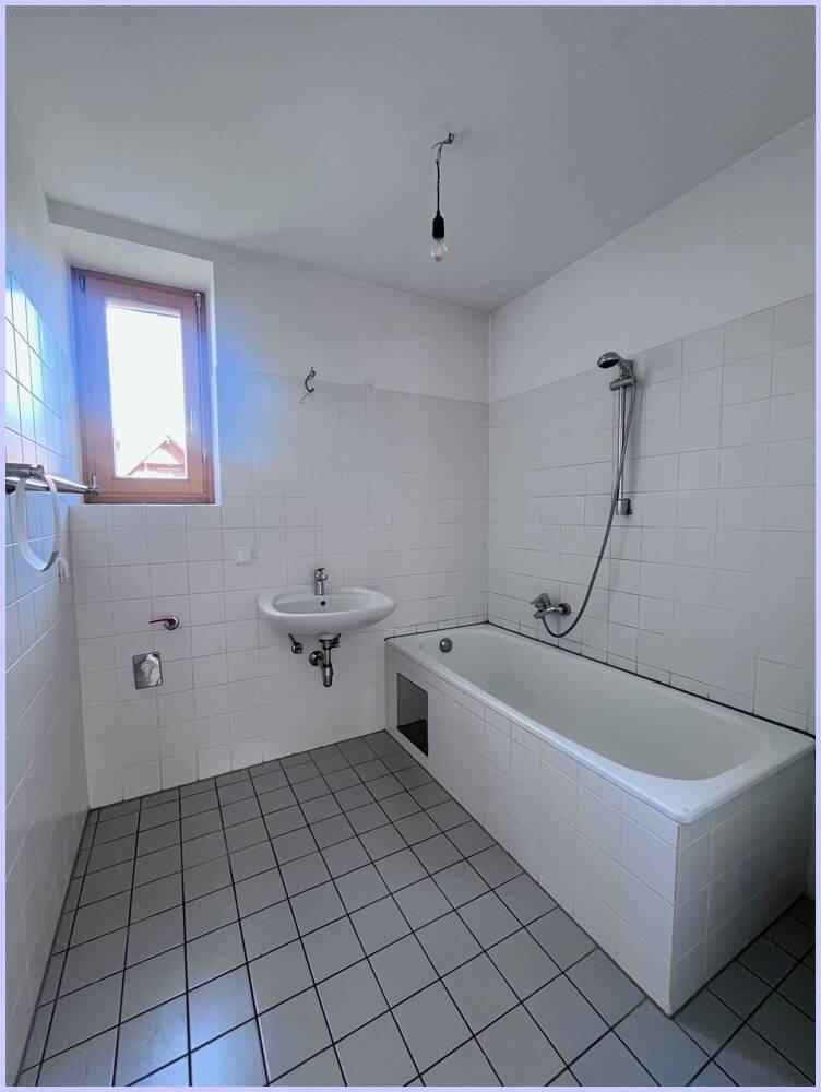Badezimmer mit Badewanne, Waschbecken und weißen Fliesen, bereit zur Modernisierung.