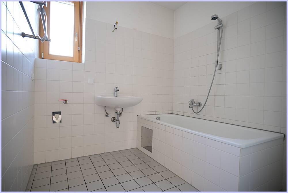 Helles Badezimmer mit Badewanne, Waschbecken und weißen Wandfliesen, mit Fenster.