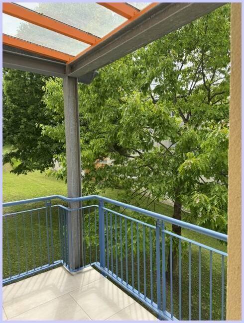 Heller Balkon mit weitem Blick auf üppiges Grün und hohe Bäume, sehr naturnah.