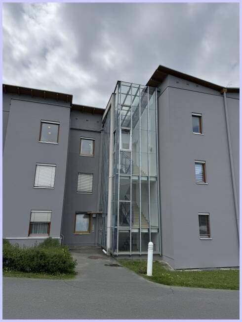 Modernes Gebäude mit grauer Fassade und markantem verglastem Treppenhaus.