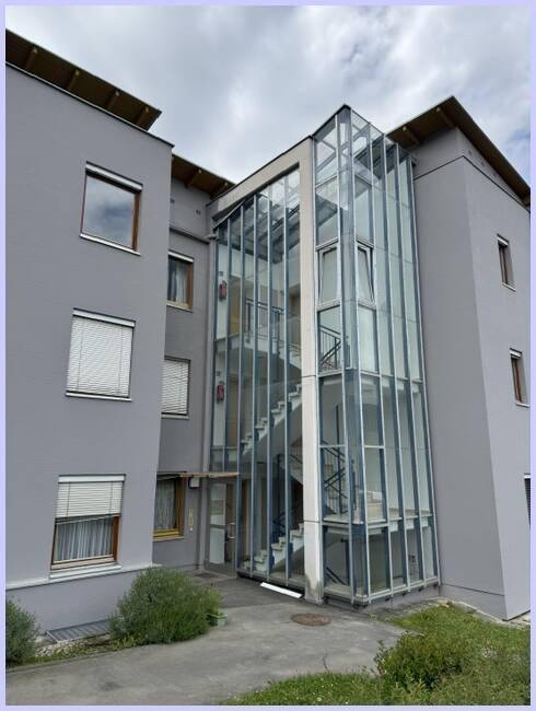 Ansicht des modernen Wohngebäudes mit auffälligem Glas-Treppenhaus und grauer Putzfassade.