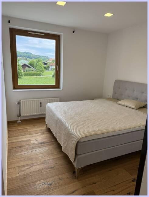 Helles Schlafzimmer mit bequemem Bett und großem Fenster mit weitem Blick ins Grüne.