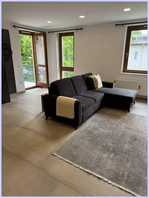 Gemütliches Wohnzimmer mit großem Ecksofa, Teppich und viel Tageslicht durch die Fenster.